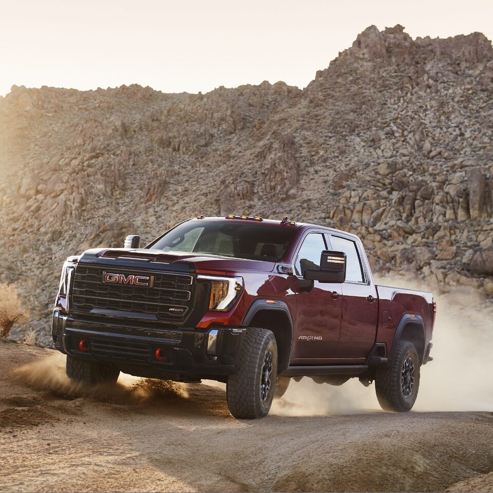 The 2024 Sierra HD AT4X driving off-road through dirt.