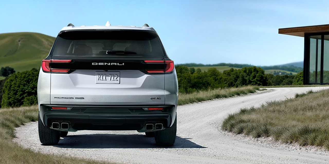 Vue arrière du GMC Acadia Denali Ultimate 2026 en mouvement vers une maison moderne.
