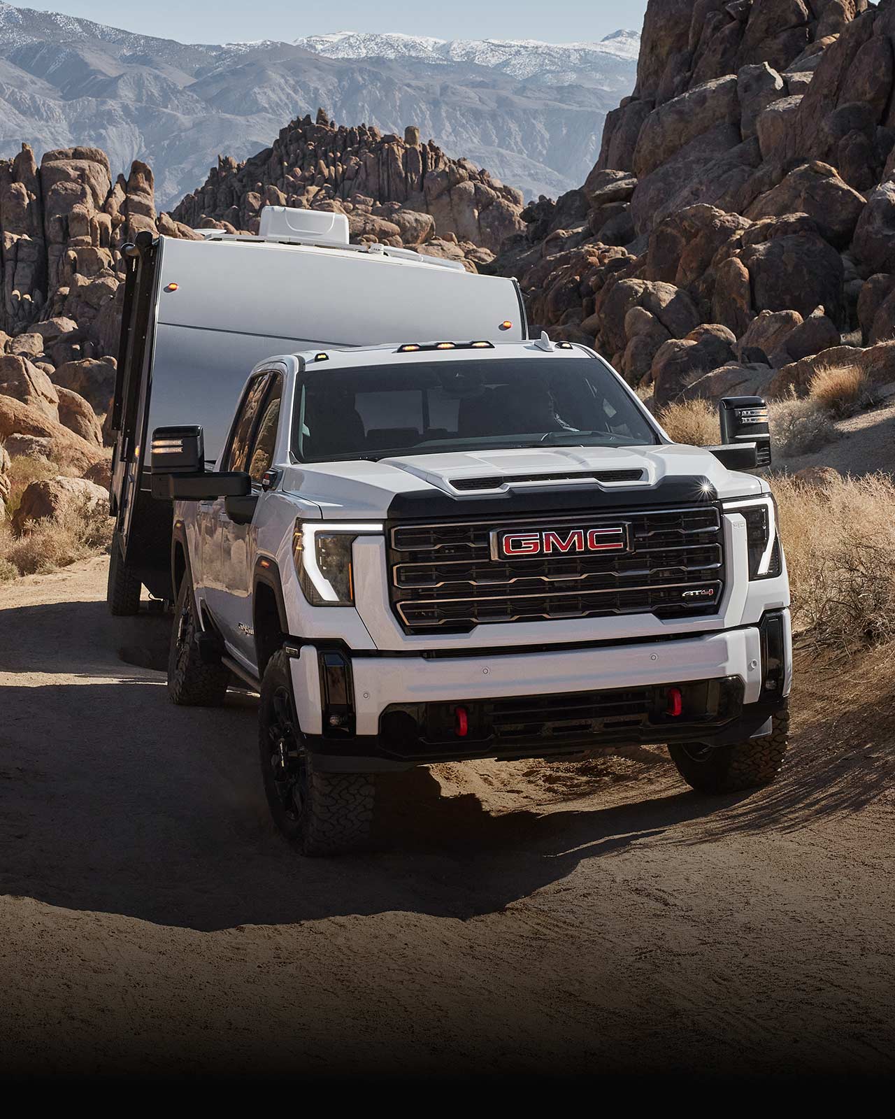GMC Sierra HD AT4X 2027 blanc remorquant une remorque blanche sur un chemin de terre rocheux.