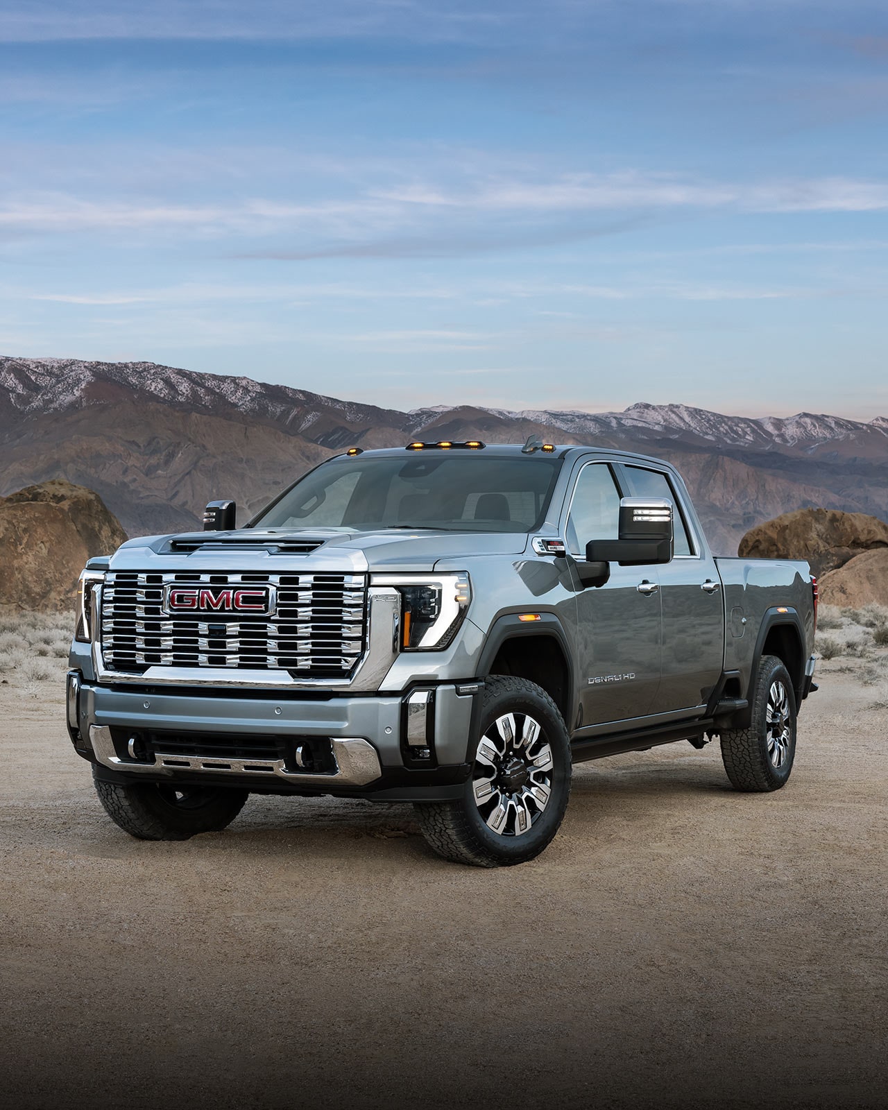 Vue avant d’un GMC Sierra HD Denali gris stationné sur un chemin de terre, avec des montagnes à l’arrière-plan.