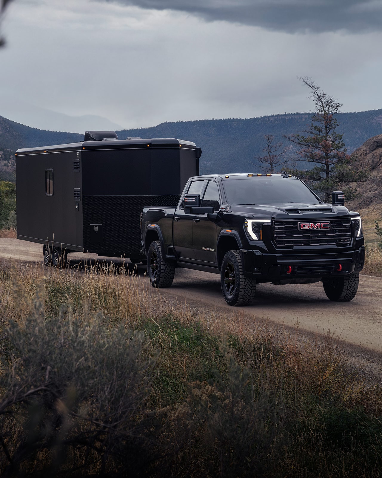 GMC Sierra HD AT4X noir remorquant une grande remorque fermée sur un chemin de terre.