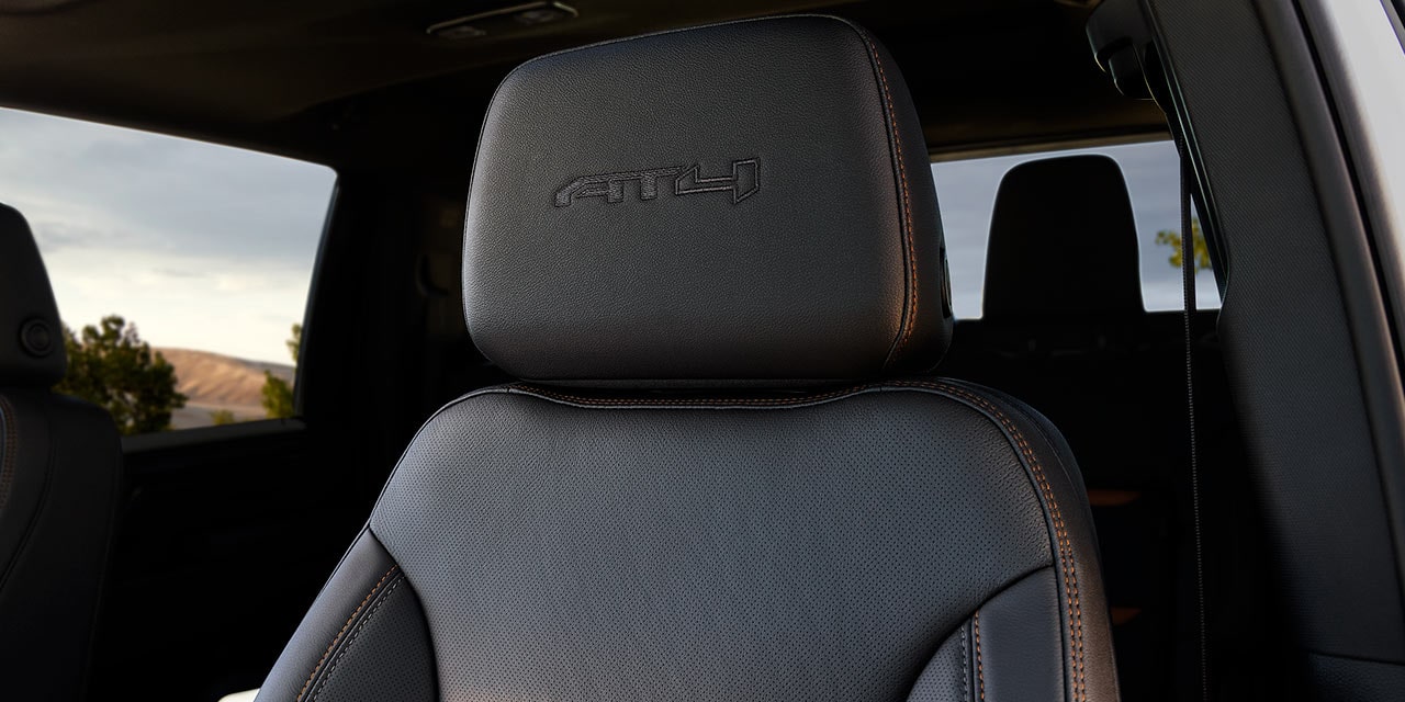 Gros plan d’un appuie-tête en cuir noir du GMC Sierra HD AT4X avec logo AT4X embossé et surpiqûres orange.