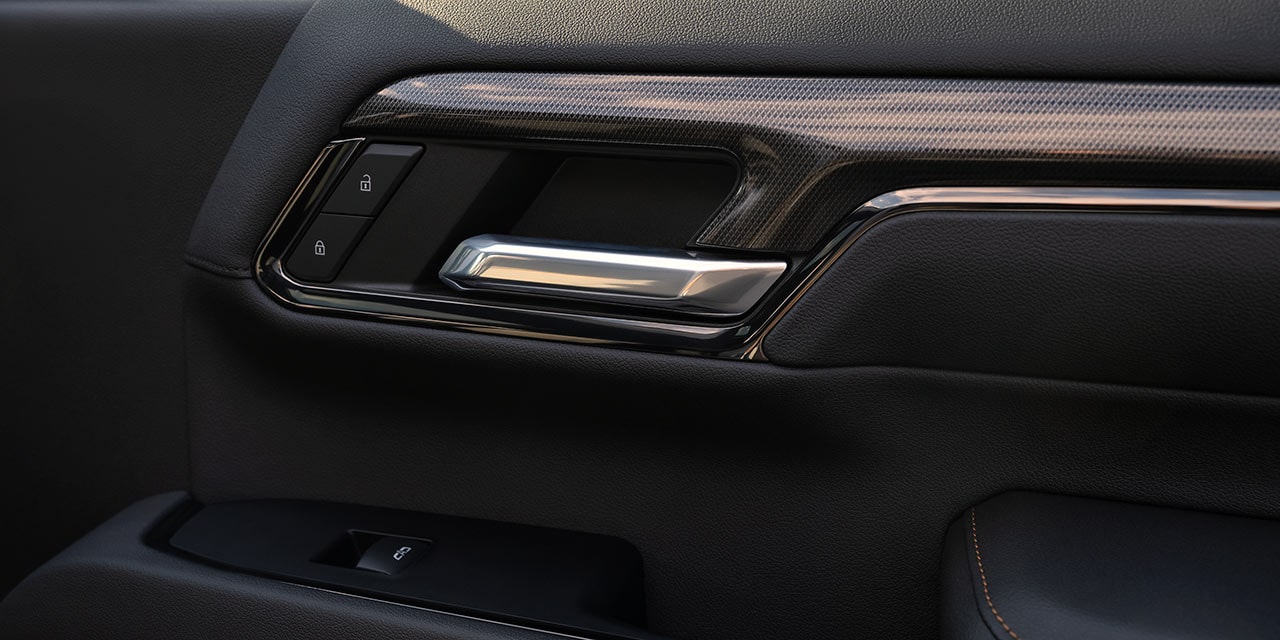 Gros plan du panneau de porte intérieur d’un GMC Sierra HD AT4X avec poignée chromée et garniture à grain de bois.