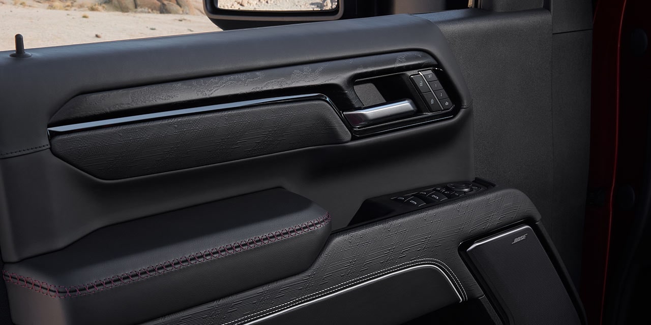 Gros plan du panneau de porte intérieur noir d’un GMC Sierra HD avec surpiqûres rouges.