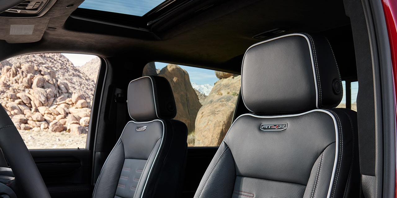 Intérieur du GMC Sierra HD AT4X avec sièges en cuir noir, toit ouvrant et paysage rocheux à l’extérieur.