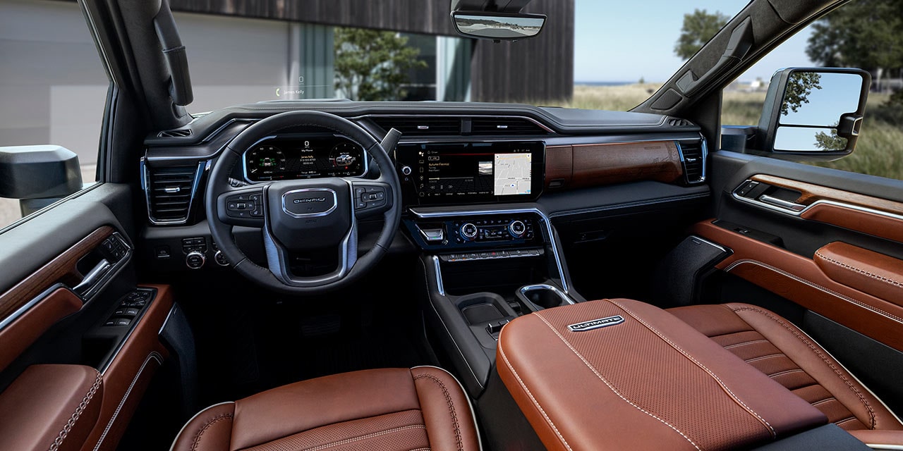Intérieur du GMC Sierra HD 2027 avec sièges en cuir brun et maison moderne visible à l’arrière-plan.