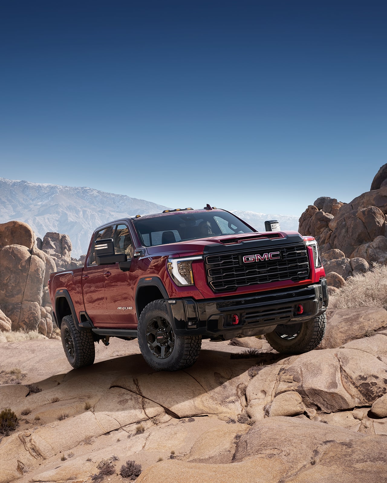 GMC Sierra HD AT4X 2027 rouge roulant dans un paysage désertique rocheux.