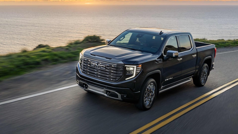 2023 Sierra Denali Ultimate driving down a road at dusk.
