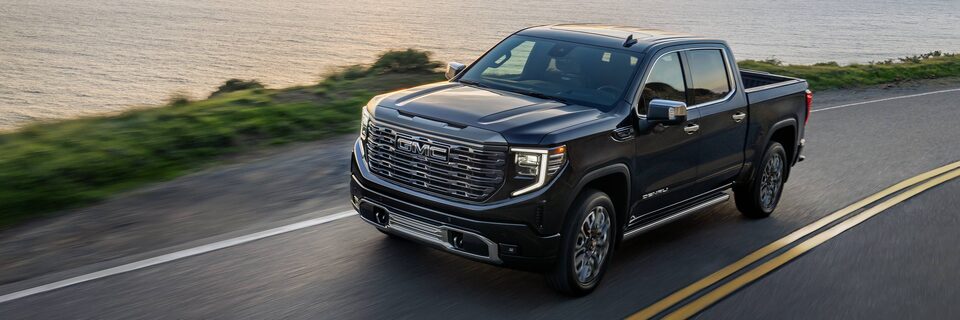 2023 Sierra Denali Ultimate driving down a road at dusk.