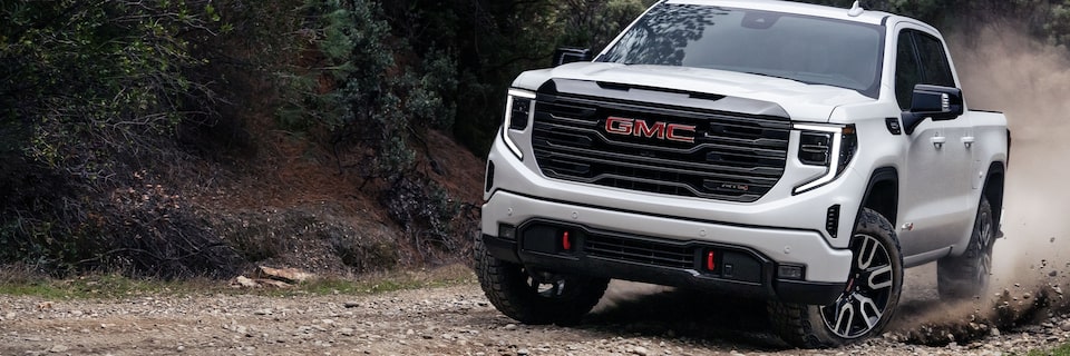 The 2024 GMC Sierra 1500 AT4 driving on a tree-lined dusty road.