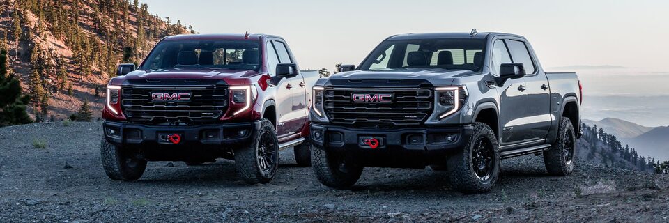 Two models of the 2024 Sierra 1500 AT4 parked on a cliffside.