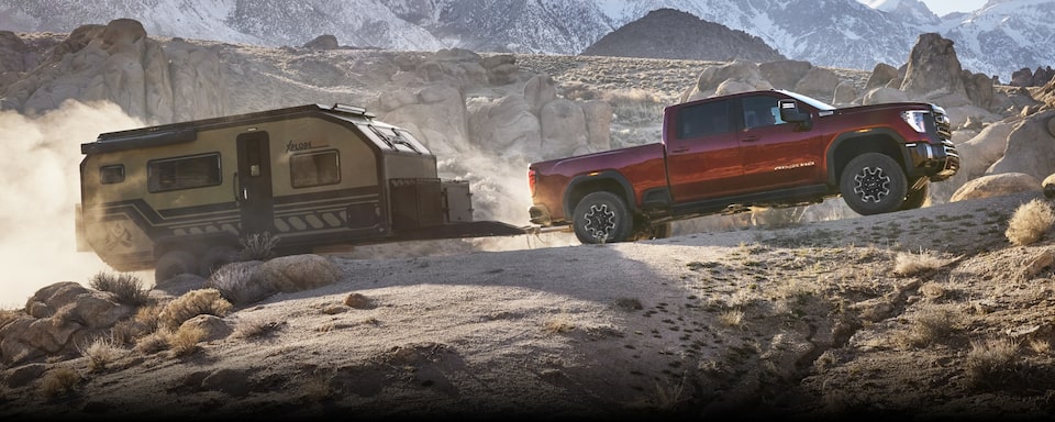 The New 2024 GMC Sierra HD easily hauling a trailer through rocky terrain.