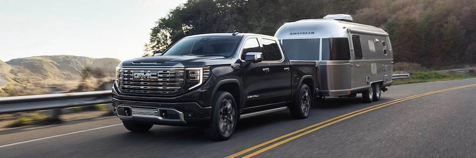  The 2024 GMC Sierra 1500 Denali with a trailer attached while driving on the road.