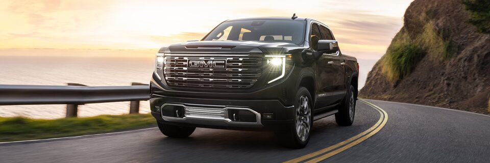 The 2024 GMC Sierra 1500 Denali driving on a road by the sea.