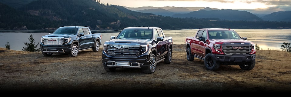 Three models of the 2024 GMC Sierra 1500 parked on the lakeside.