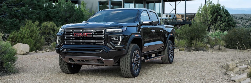 Vue latérale avant d’un GMC Canyon Denali 2025 stationné devant un chalet moderne dans les montagnes.