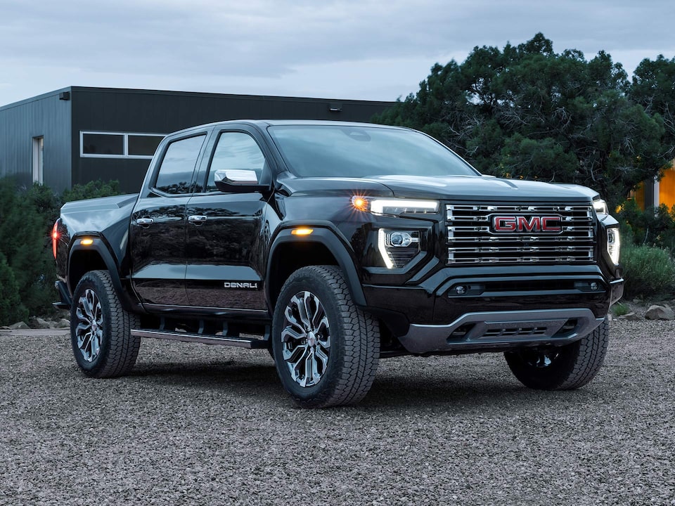 Vue latérale avant d’un GMC Canyon Denali 2025 stationné avec les phares allumés.