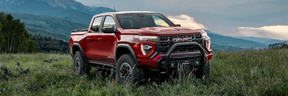 Front-side view of a red 2025 GMC Canyon AT4 parked in a grassy field.