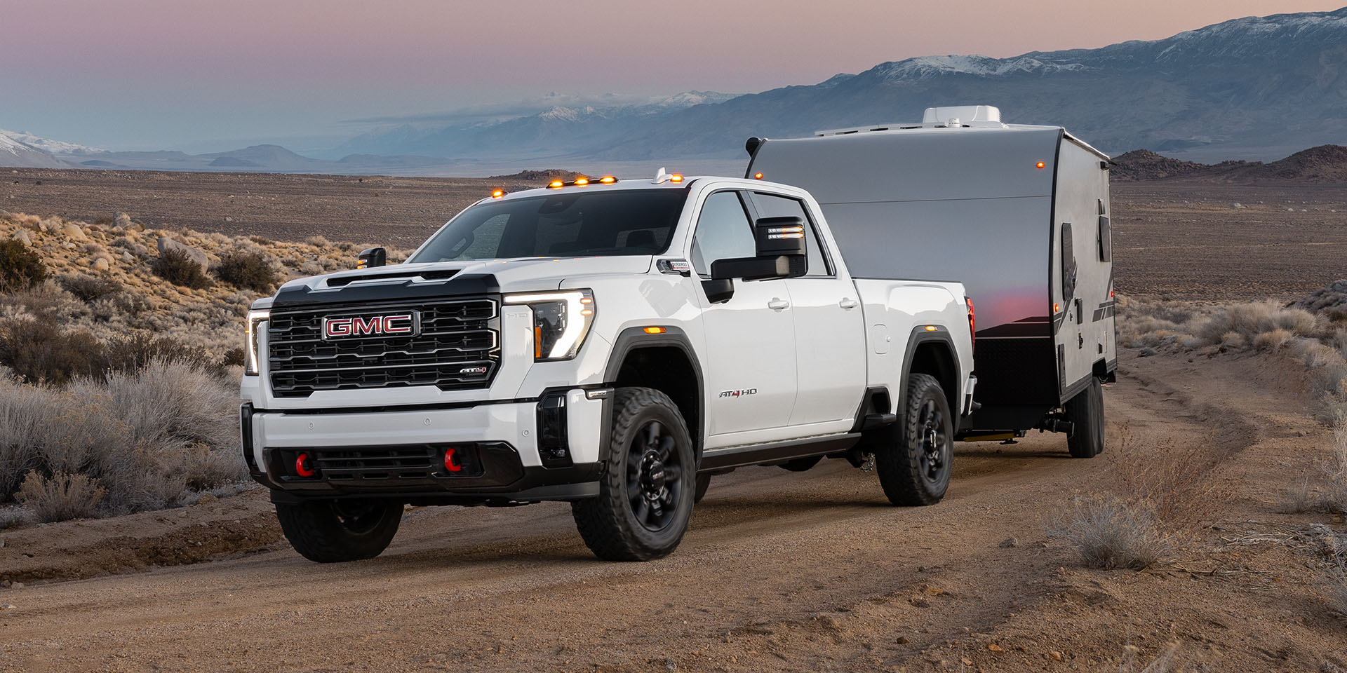 A 2026 GMC Sierra HD AT4 Truck Hauling a Trailer Through the Desert at Dusk.