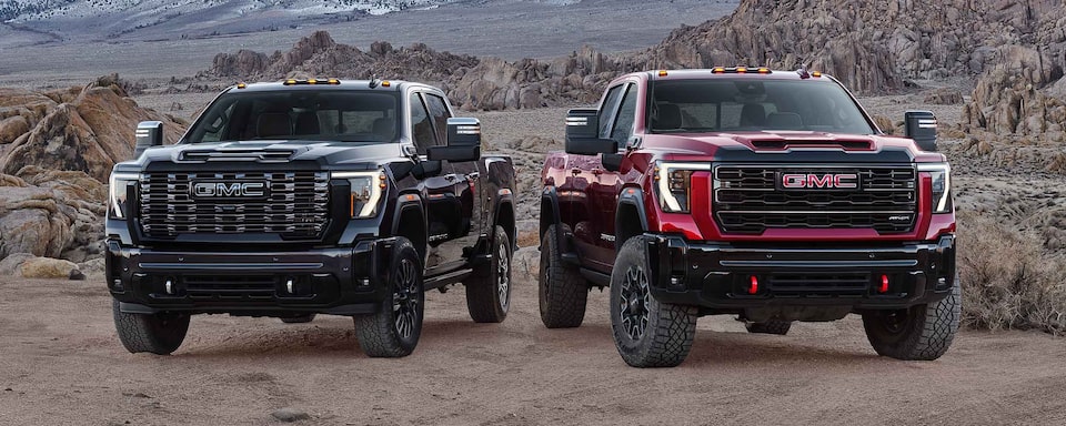 Two 2025 GMC Sierra HD Trucks Parked Side by Side with Mountains in the Background.