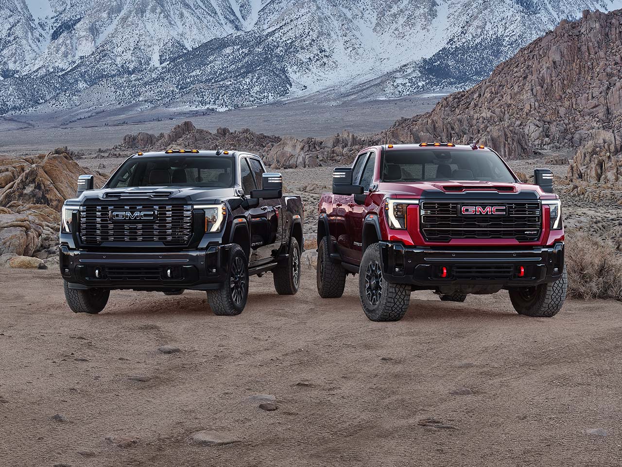 Deux camions GMC Sierra HD 2025 stationnés côte à côté avec des montagnes en arrière-plan.