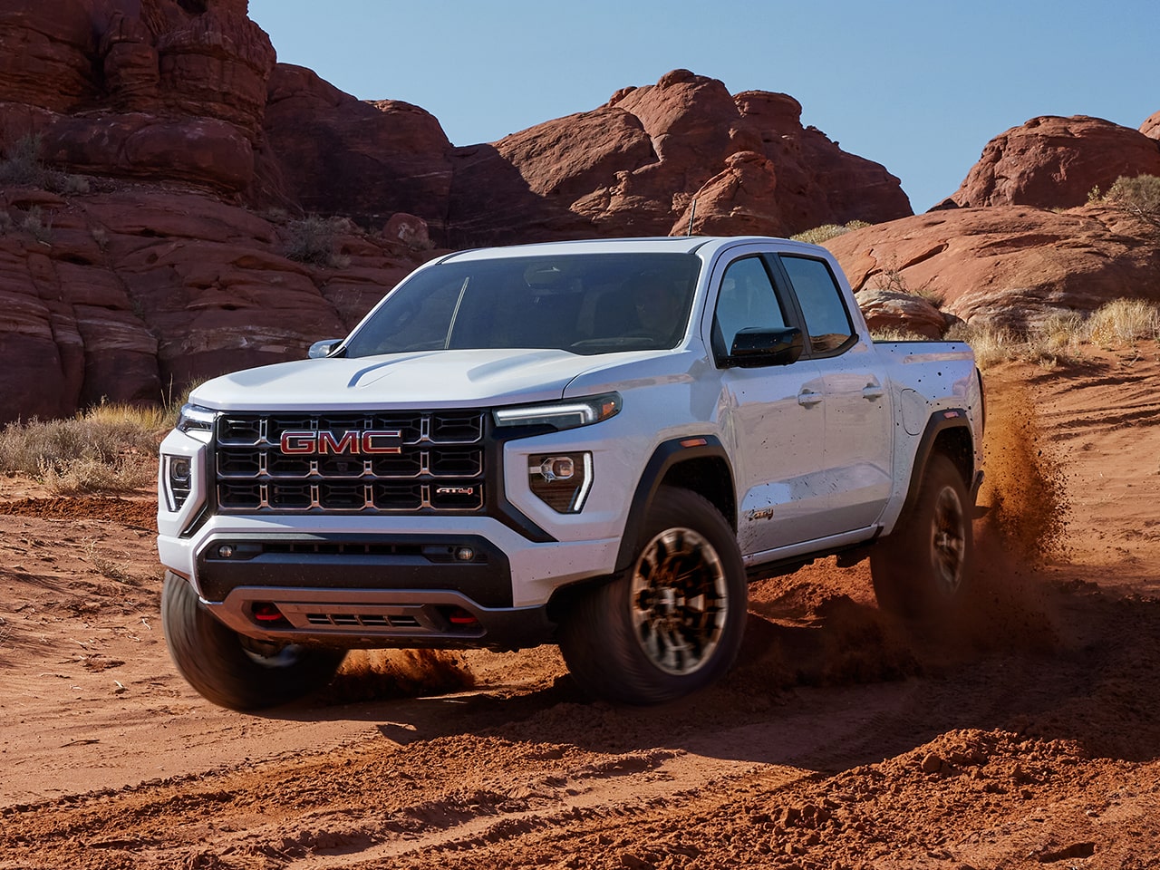 Vue latérale avant du GMC Canyon AT4 2026 en mouvement seul sur un terrain rocailleux.