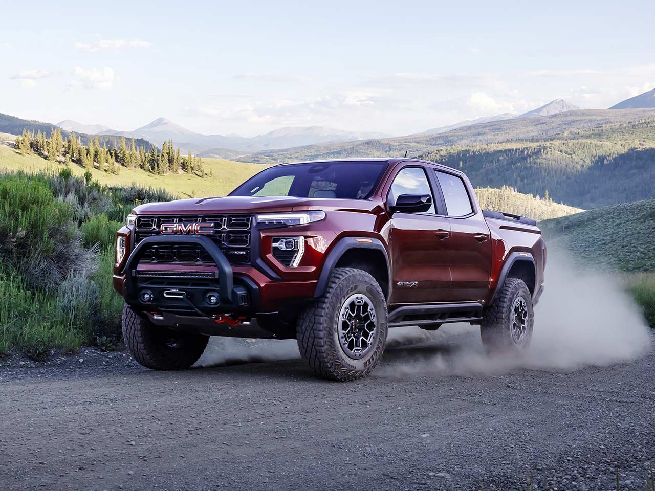 Vue latérale avant du GMC Canyon AT4X 2026 qui roule à toute allure sur une route de campagne.