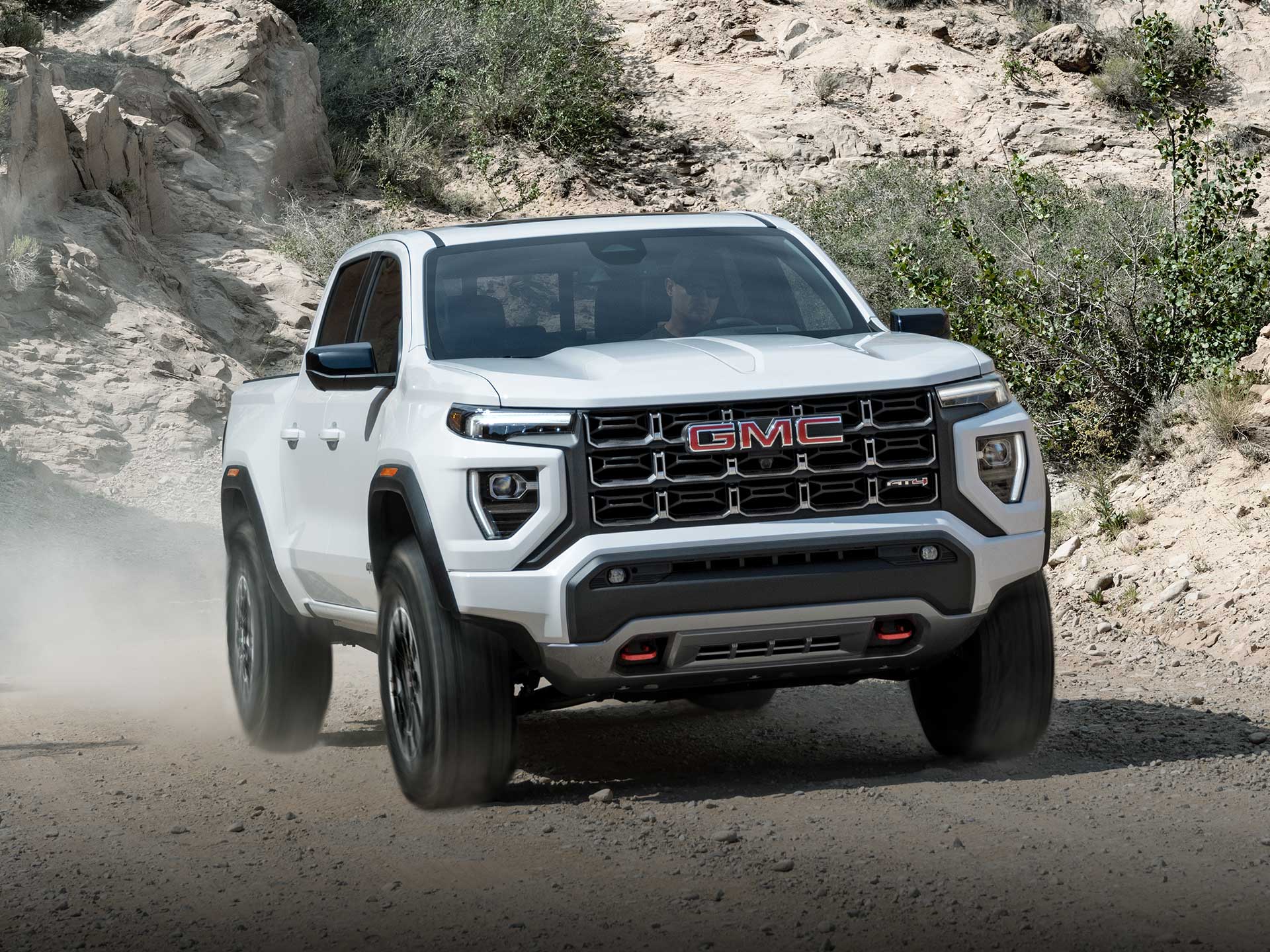 Vue latérale avant du GMC Canyon AT4 2026 en mouvement seul sur une route de montagne.