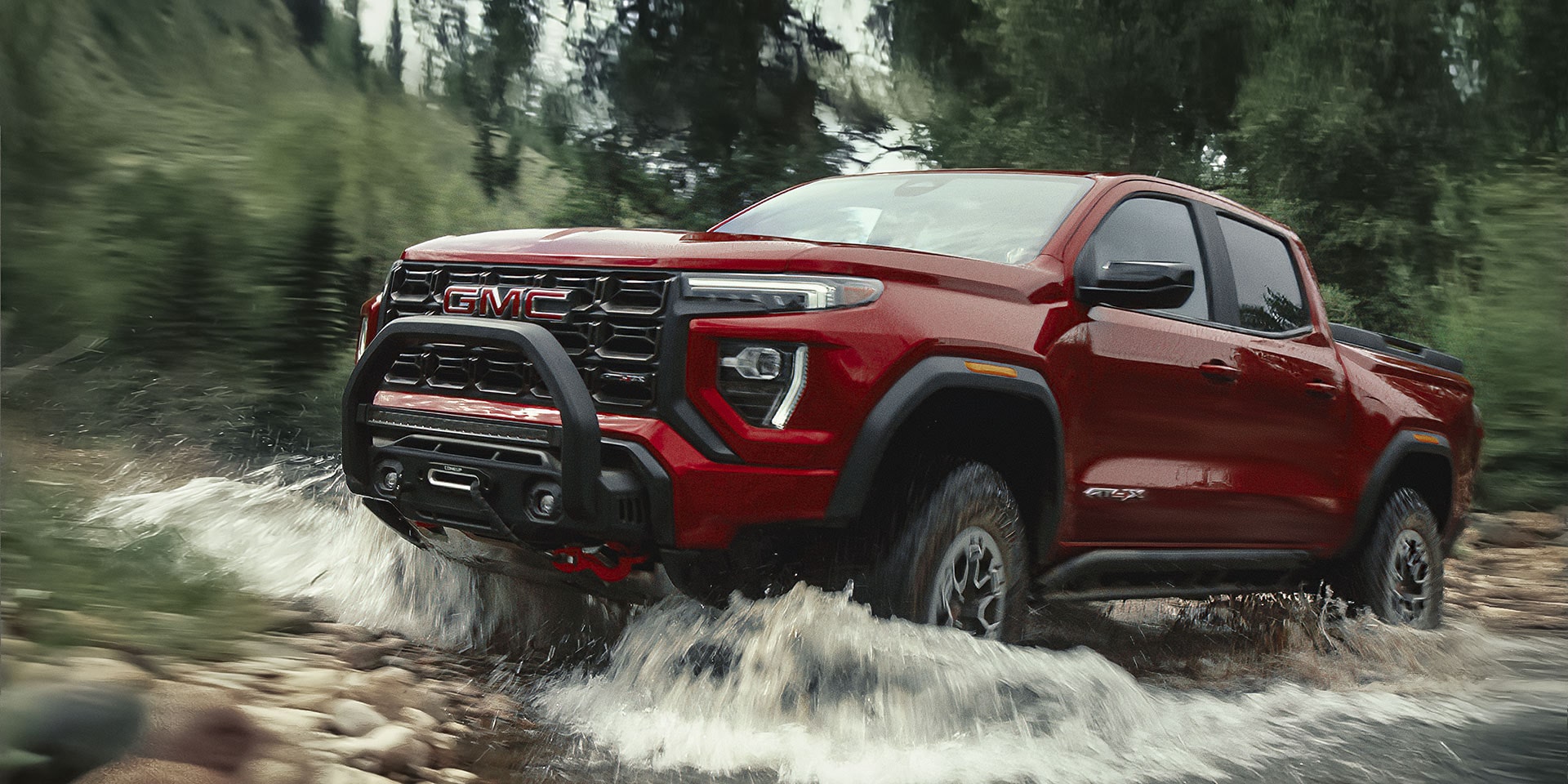 Front-side view of the 2026 GMC Canyon driving through a flooded area in the forest.