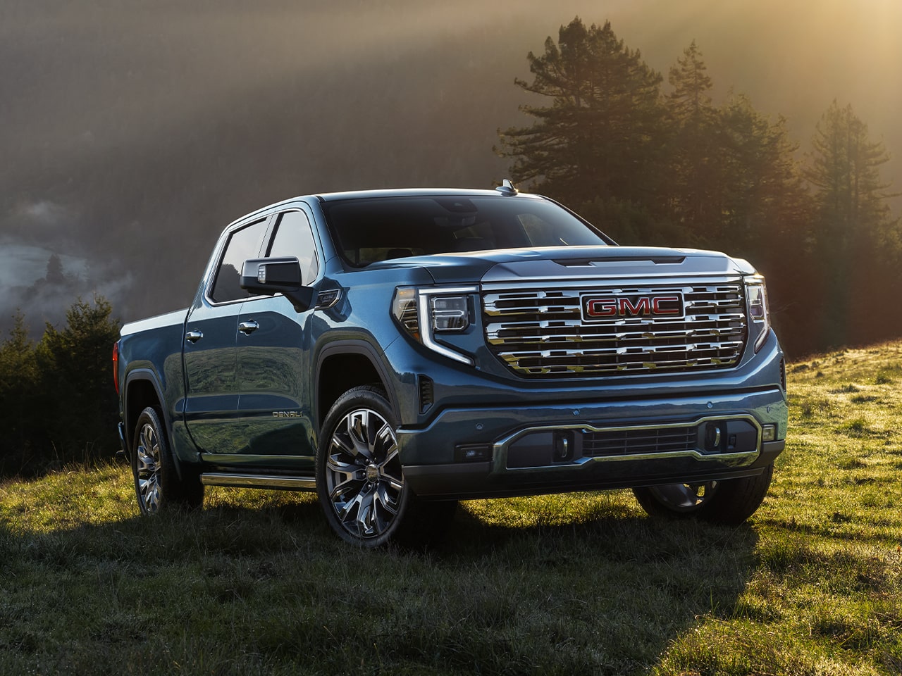 Vue latérale avant du pick-up GMC Sierra 1500 2026 stationné dans une vallée verdoyante au lever du soleil.
