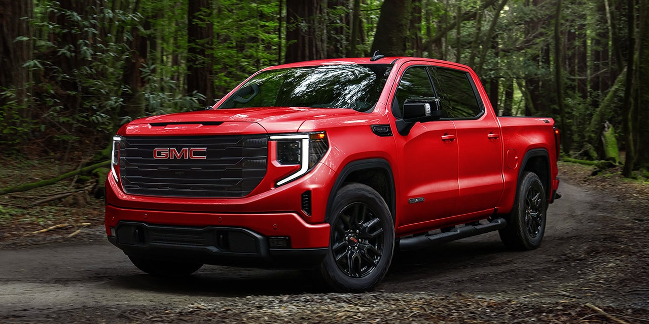 Front Three-Quarters View of a Red 2026 GMC Sierra 1500 Parked in a Green Forest.