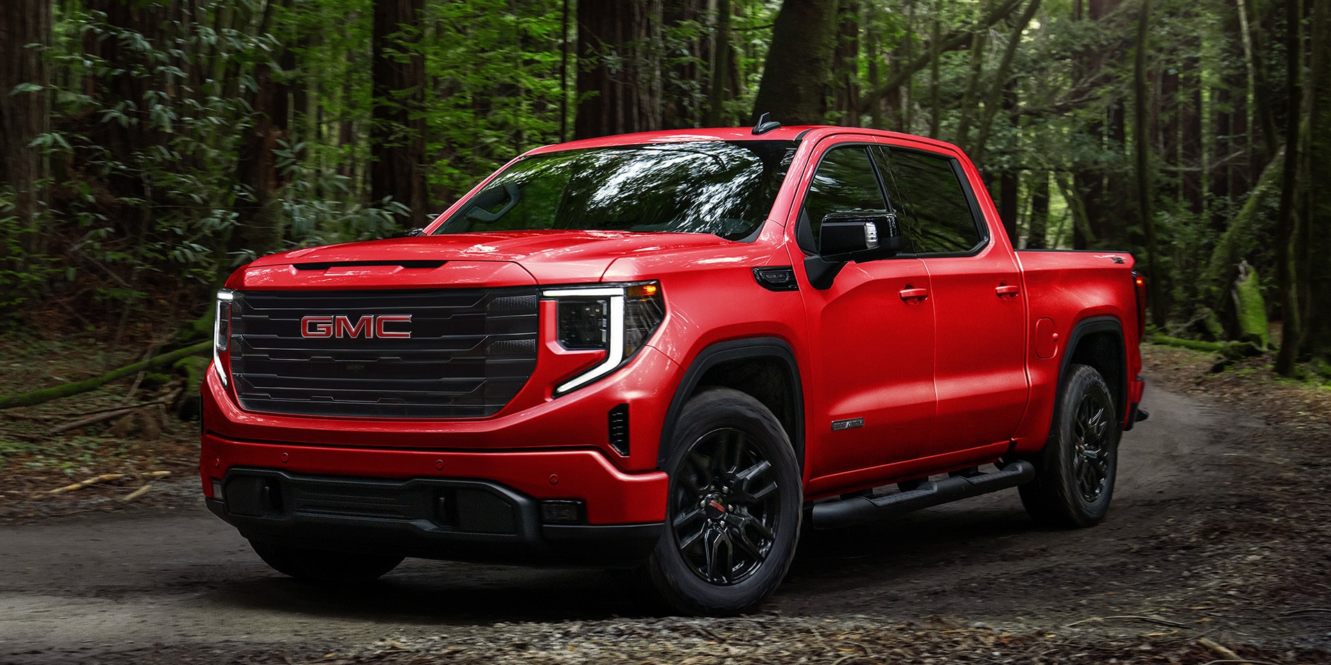 Front Three-Quarters View of a Red 2026 GMC Sierra 1500 Pro Parked in a Green Forest.