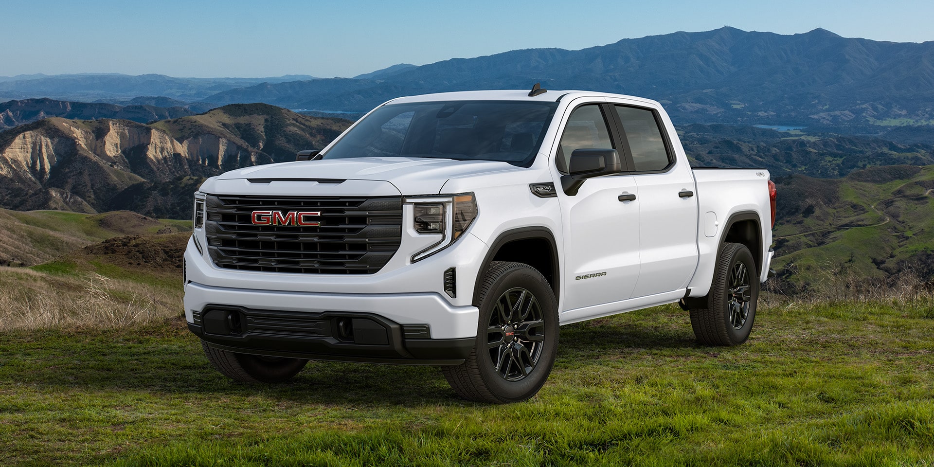 Front Three-Quarters View of a White 2026 GMC Sierra 1500 Pro Parked in a Green Valley.