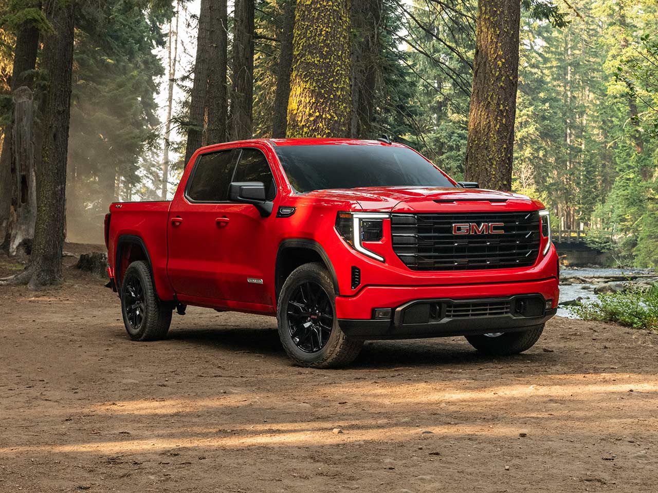 Front Three-Quarters View of a Red 2026 GMC Sierra 1500 Parked in a Forest.