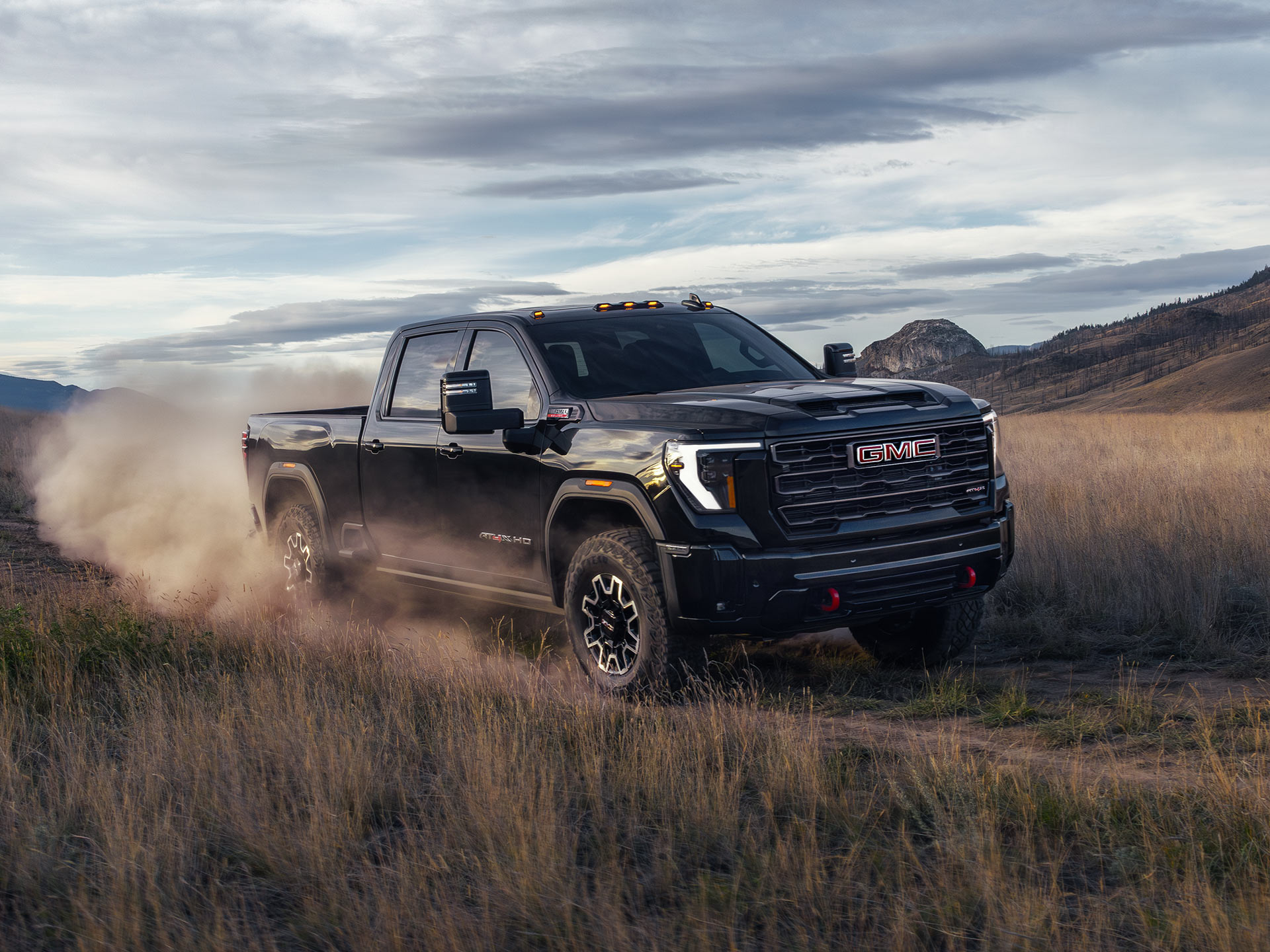 Front-side view of the 2026 GMC Sierra HD AT4 driving alone on a dirt path.