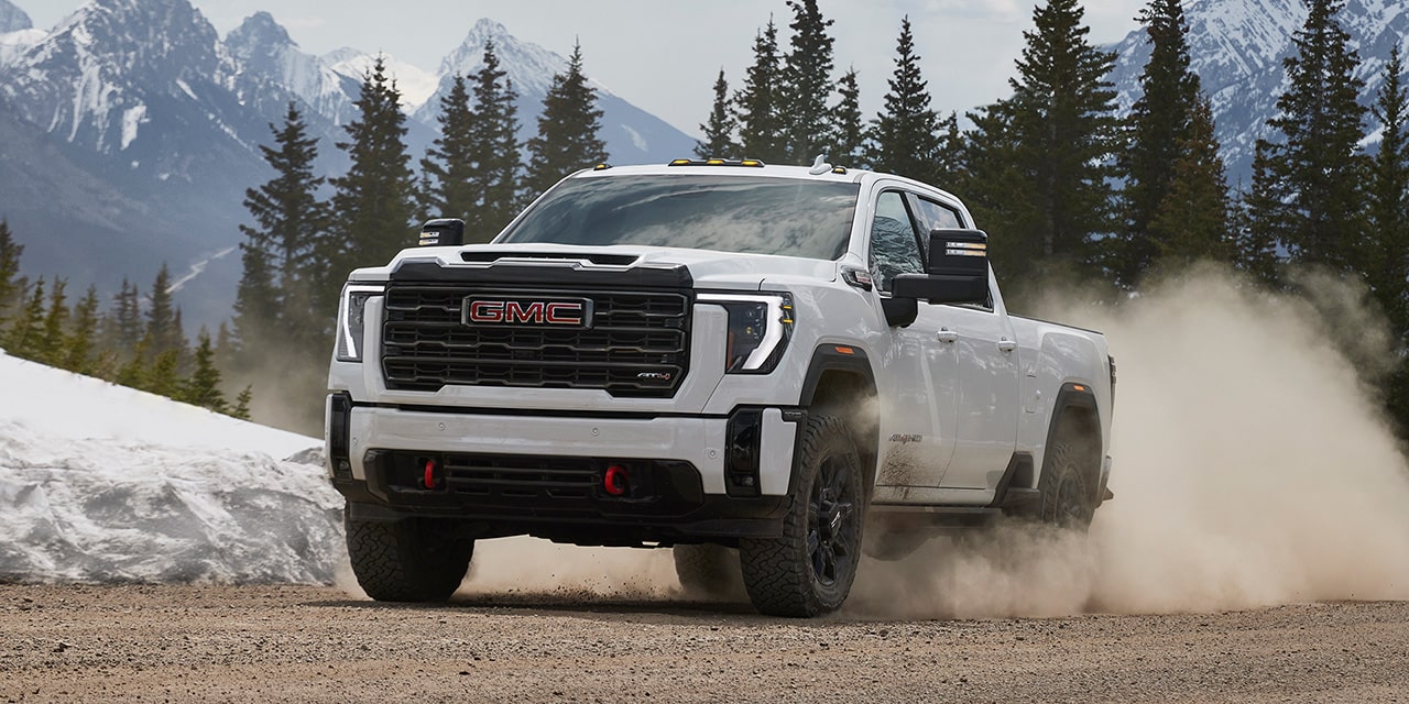 Front Three-Quarters View of a White 2026 GMC Sierra HD AT4 Truck Driving Through the Mountains Kicking Up Dirt