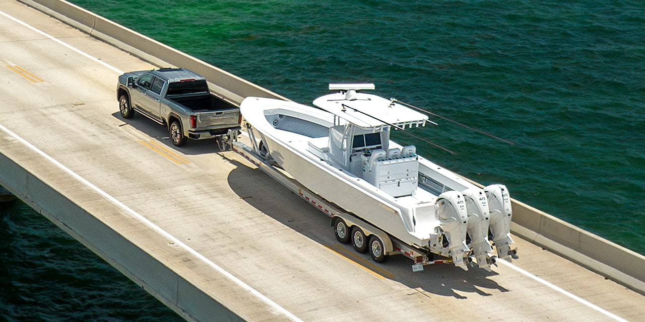 Three-Quarters Birdseye View of a 2026 GMC Sierra HD Denali Hauling a Boat on an Open Road Near a Lake.