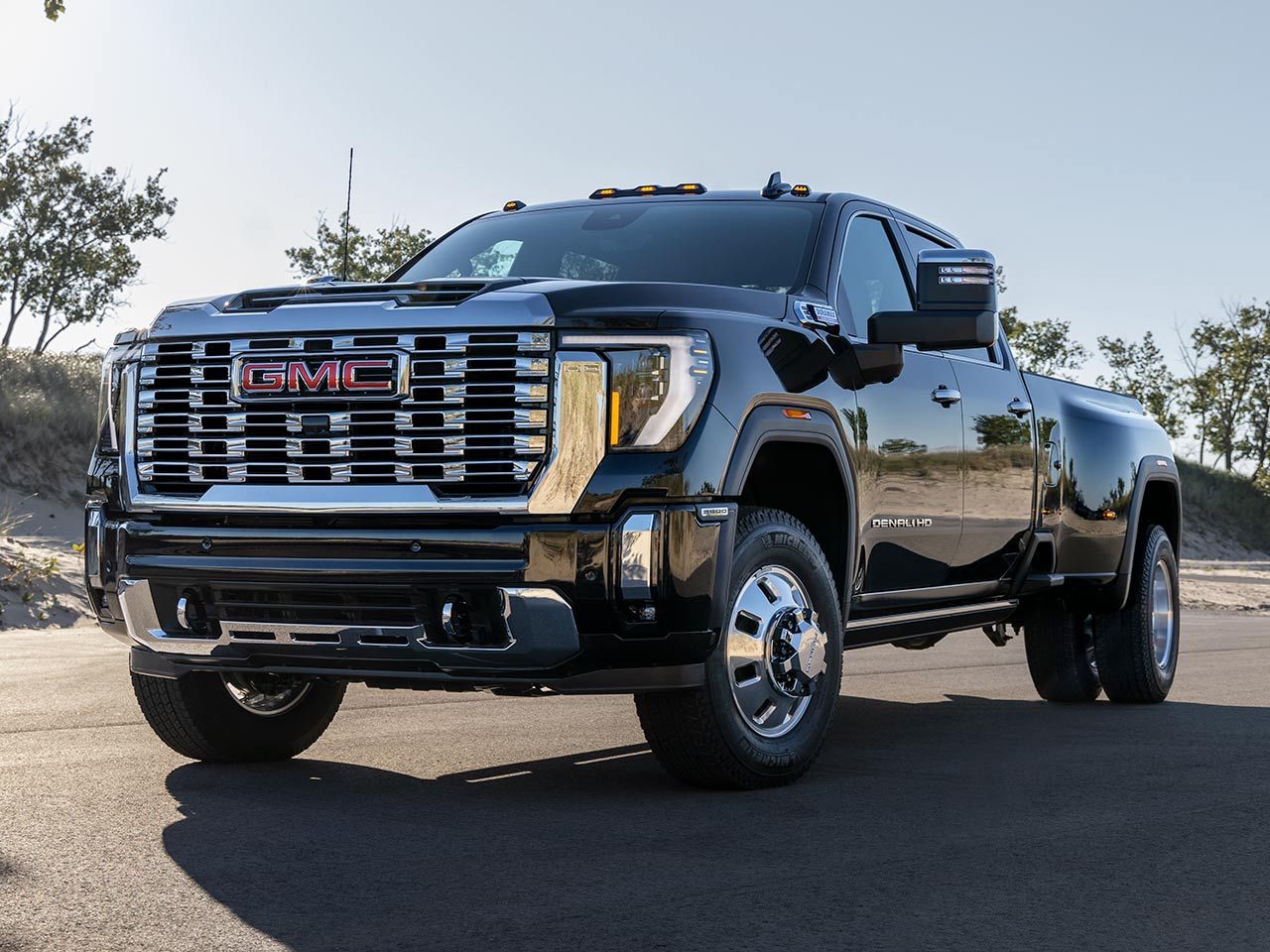 Wide Front Three-Quarters View of a 2026 GMC Sierra HD Denali Luxury Truck Driving on an Open Road.