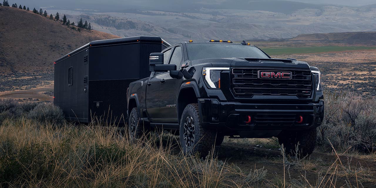 The 2026 GMC Sierra HD Truck Towing a Trailer Through a Hillside road.