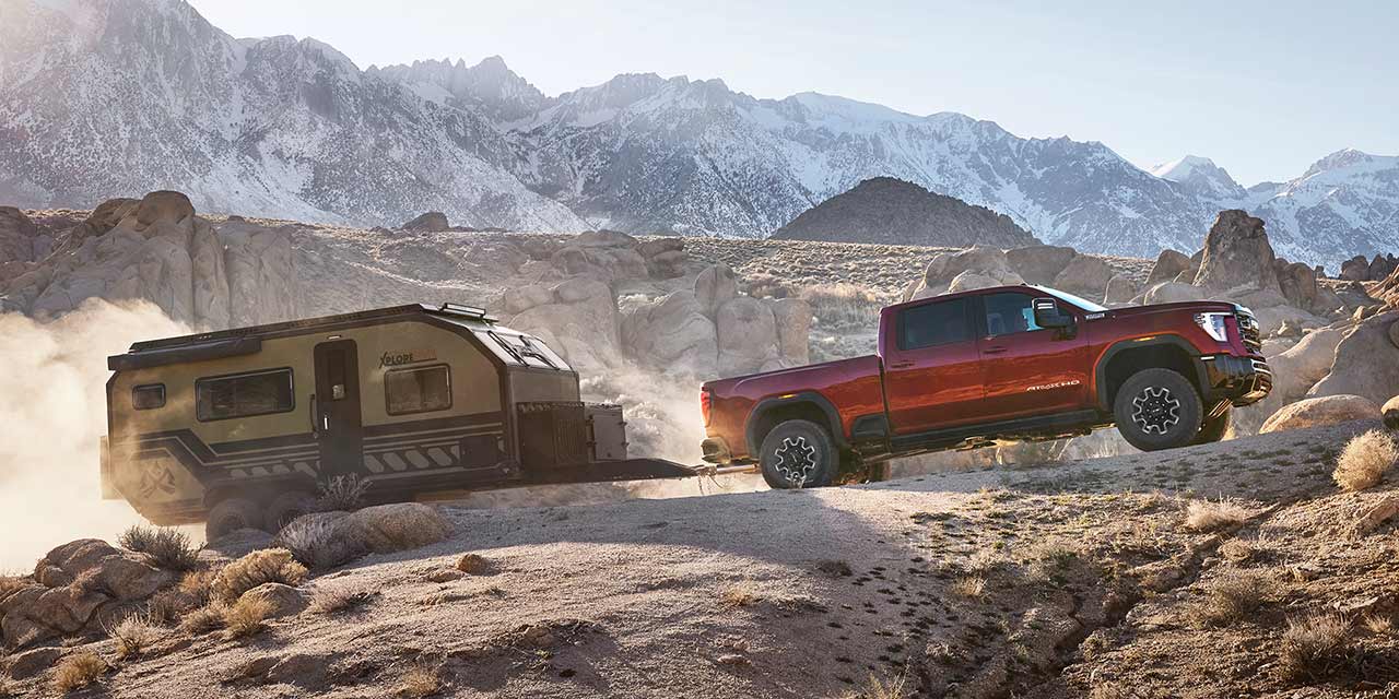 Side View of the 2026 GMC Sierra HD Truck Hauling a Trailer on a Rocky Mountain Road.