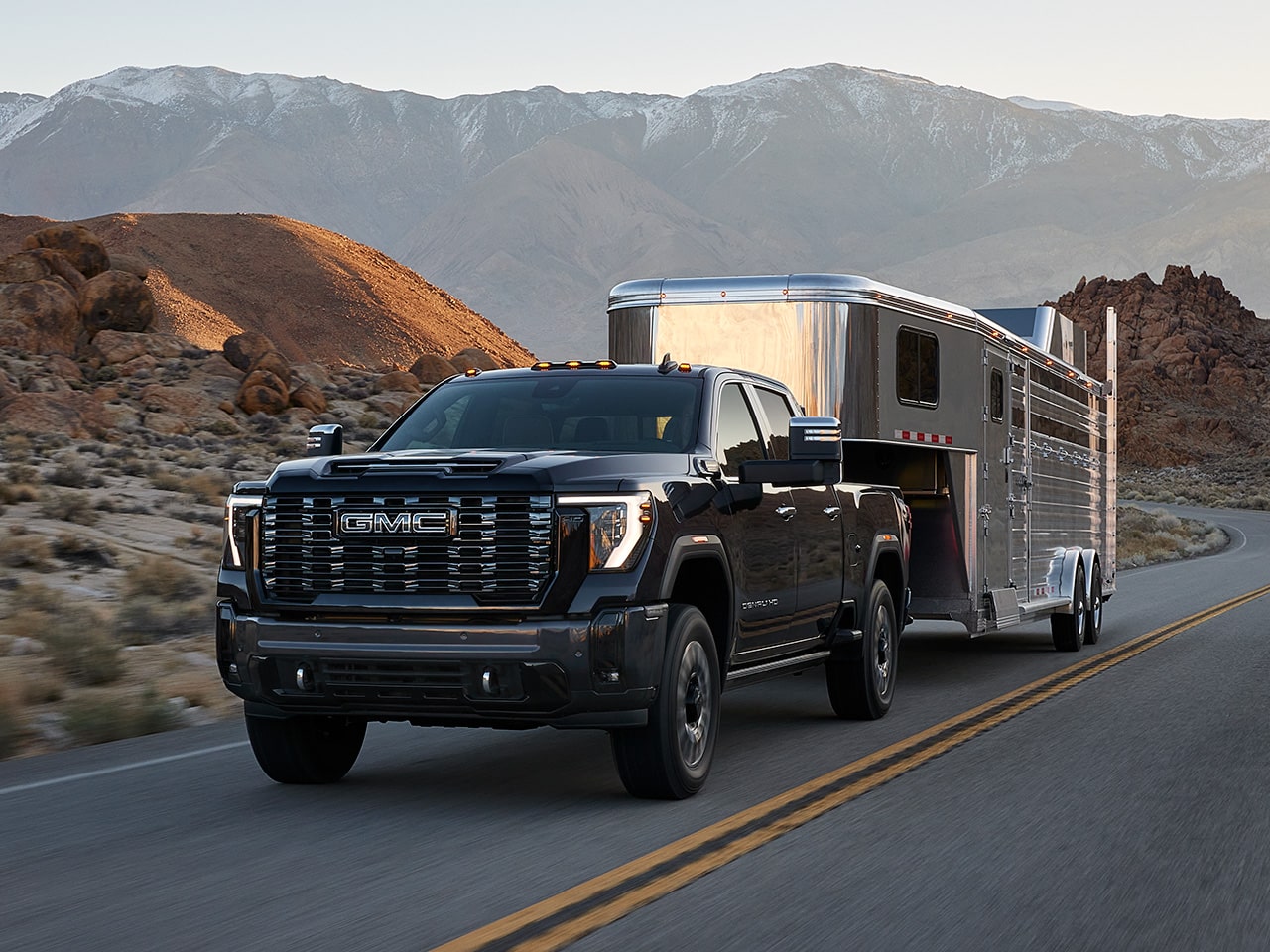 The 2026 GMC Sierra HD Pro Truck Towing a Trailer Down a Mountain Lined Road.
