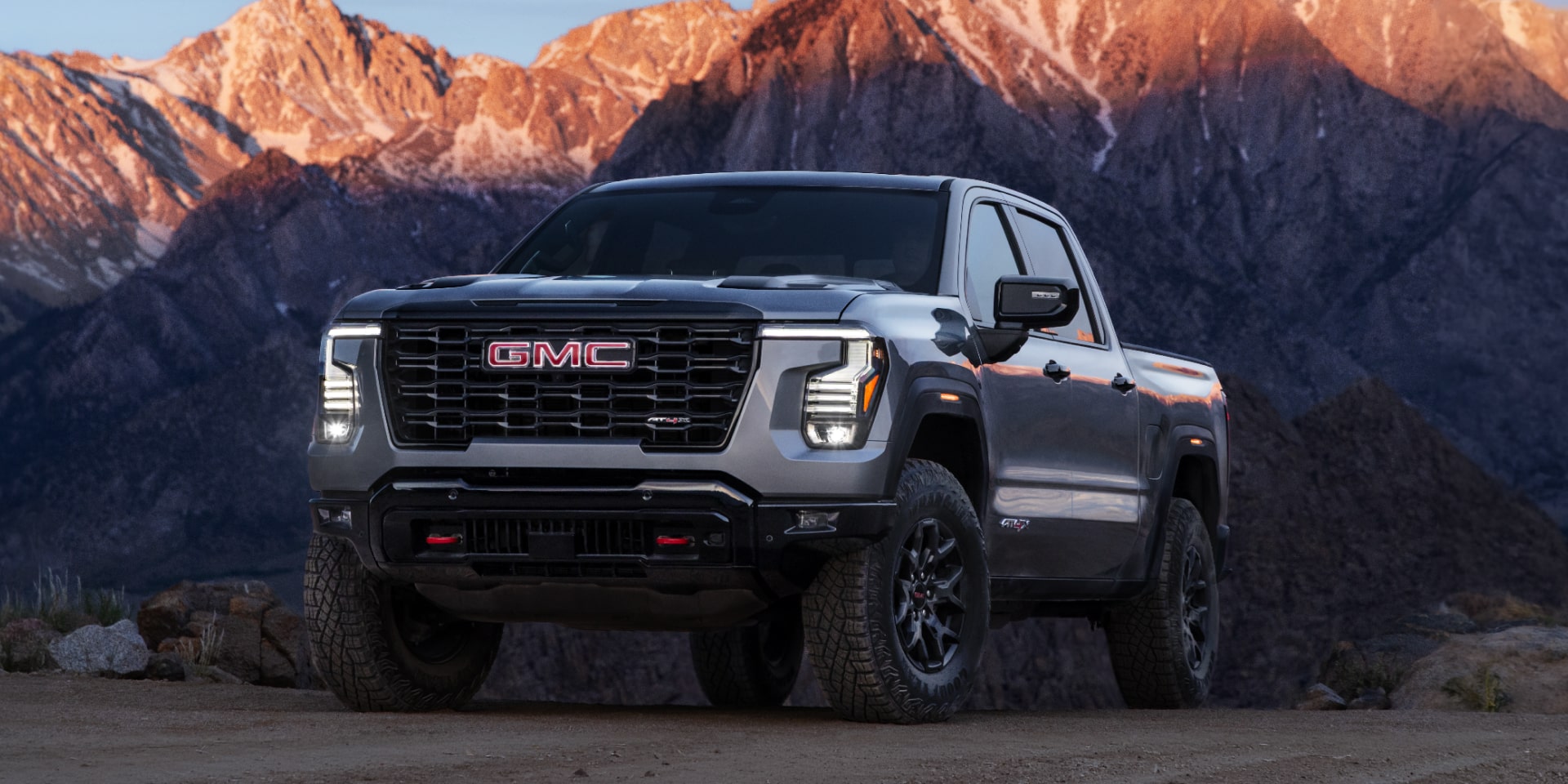 GMC Sierra 1500 2027 gris stationné sur un chemin de terre avec des montagnes en arrière-plan