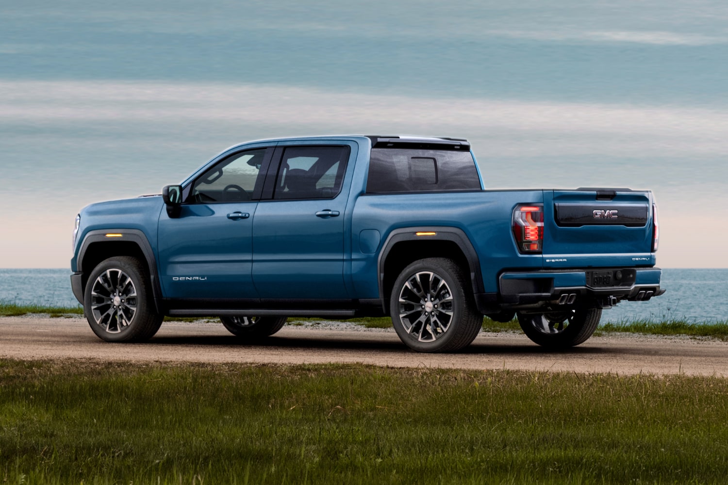 Vue de côté d’un GMC Sierra 1500 Denali bleu stationné sur un chemin herbeux au bord de l’océan
