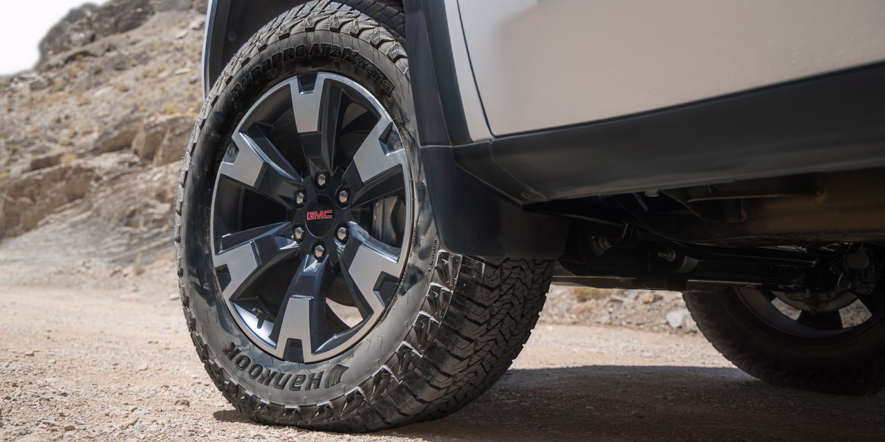 Gros plan sur la roue avant d’un GMC Sierra 1500 AT4X blanc avec pneu robuste sur un chemin de terre