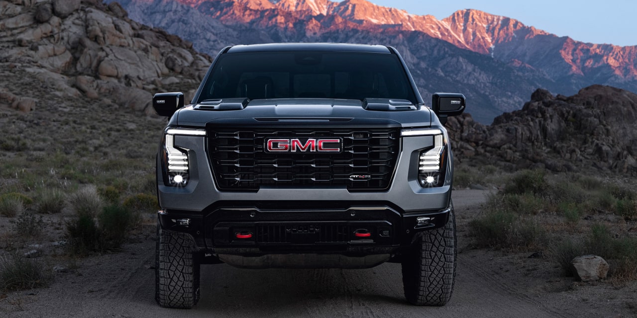 Vue de face d’un GMC Sierra 1500 AT4X gris stationné sur un sentier de terre avec des montagnes en arrière-plan