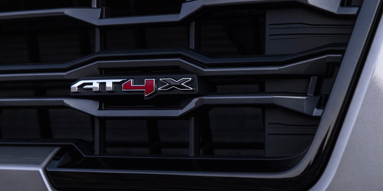 Gros plan sur la calandre noire d’un GMC Sierra 1500 avec écusson AT4X argent et rouge
