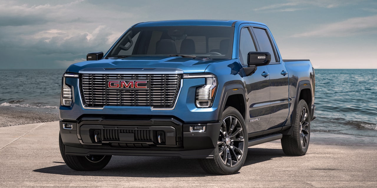 Vue de trois quarts avant d’un GMC Sierra 1500 Denali bleu stationné sur une plage avec l’océan en arrière-plan