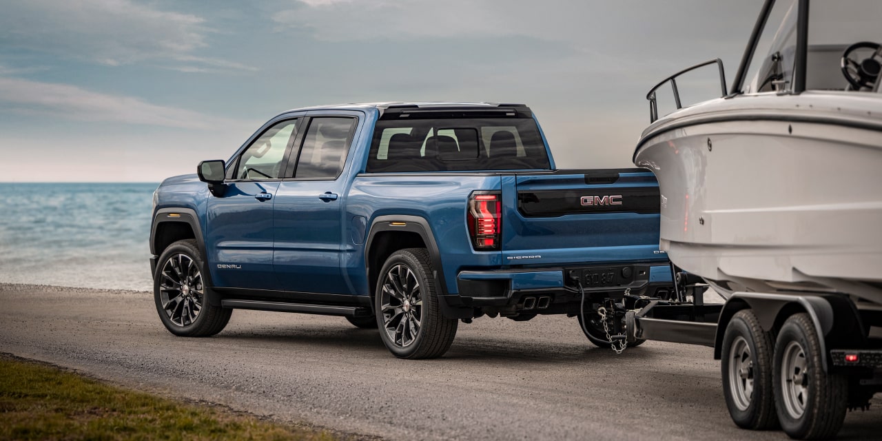 Vue de trois quarts arrière d’un GMC Sierra 1500 Denali bleu remorquant un bateau blanc au bord de l’eau