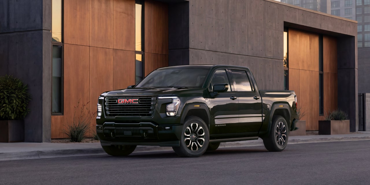 Vue de trois quarts avant d’un GMC Sierra 1500 vert métallisé foncé stationné devant un bâtiment moderne