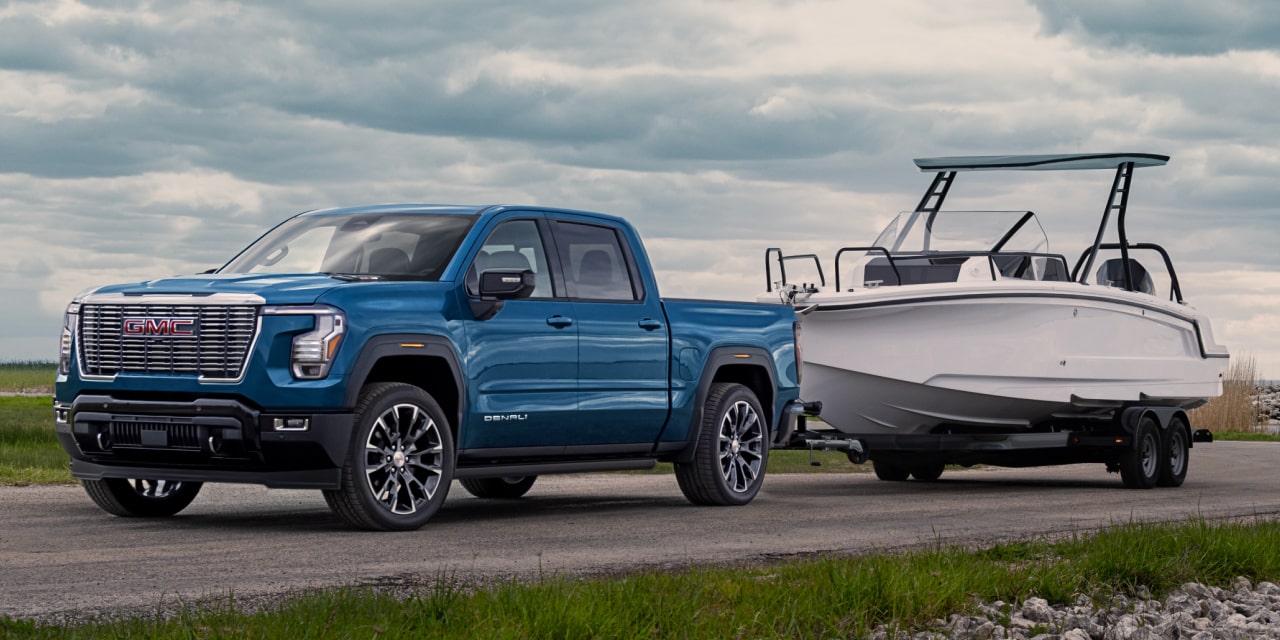GMC Sierra 1500 Denali 2027 bleu remorquant un bateau blanc sur une route sous un ciel nuageux